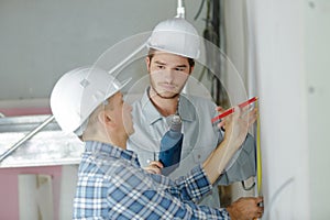 Builder and appentice measuring wall with tape measure