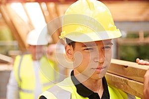 Builder And Apprentice Carrying Wood On Construction Site