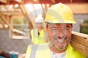 Builder And Apprentice Carrying Wood On Construction Site