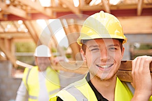 Builder And Apprentice Carrying Wood On Construction Site