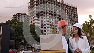 A builder and an architect with a laptop are standing at a construction site.