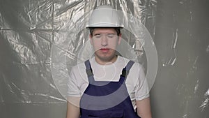 Builder in blue overalls puts on white hard hat helmet