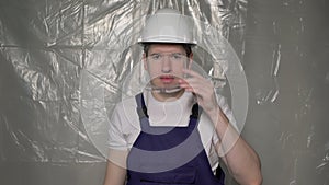 Builder in blue overalls puts on white hard hat helmet