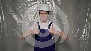 Builder in blue overalls puts on white hard hat and shows thumbs up.