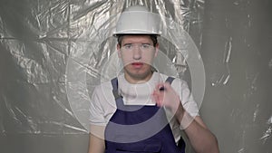 Builder in blue overalls puts on white hard hat and shows thumbs up.