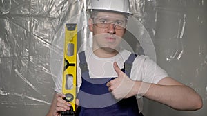 Builder in blue overalls and white hard hat helmet and glasses with level.