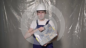 Builder in blue overalls and white hard hat helmet and glasses with toolbox.