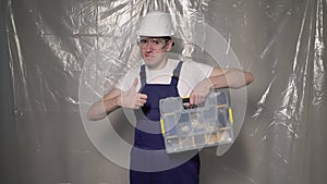 Builder in blue overalls and white hard hat helmet and glasses with toolbox.