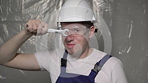 Builder in blue overalls and white hard hat helmet and glasses with wrench.