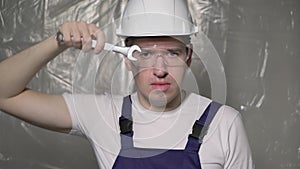 Builder in blue overalls and white hard hat helmet and glasses with wrench.