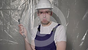 Builder in blue overalls and white hard hat helmet and glasses with wrench.