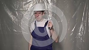 Builder in blue overalls and white hard hat helmet and glasses with wrench.