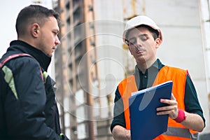 Builder briefing to achritector in hardhats with tablet pc computer outdoors