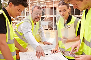 Builder On Building Site Discussing Work With Apprentice