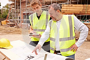 Builder On Building Site Discussing Work With Apprentice