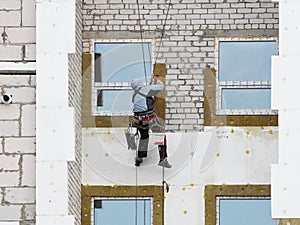 A builder in climbing equipment insulates the facade of a high-rise building with foam plastic. Safety measures for high-altitude