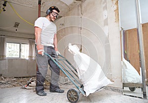 Builder collecting construction debris in a bag, and carrying in a hand trolley