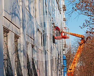 Builder in a crane basket repairs the coating of a metal structure on the wall of the facade of a building