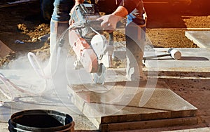 Builder cutting concrete slabs with petrol concrete saw and diamond blade during external footpath paving works close up