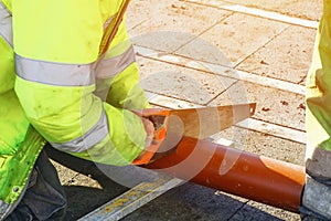 Builder cutting plastic pipe with hand saw during new house internal and external drainage system construction