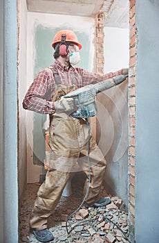 Builder with demolition hammer breaking interior wall