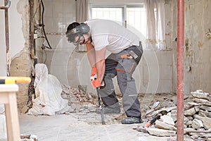 Builder digging up the house floor, lifting up old tiles with a crowbar