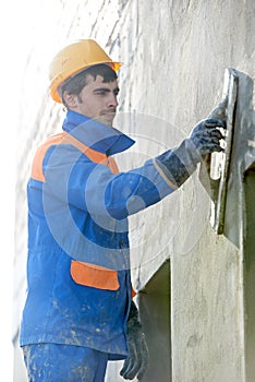 Builder at facade plastering work with putty knife float