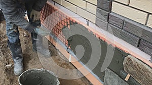 Builder faces the basement of a house with a wild stone. Flat for cladding, tabata on the construction site.