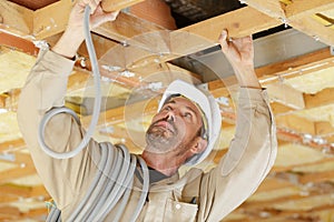 Builder feeding cable trunking into roof timbers