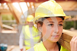 Builder And Female Apprentice Carrying Wood On Site