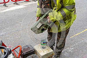 Builder filling petrol powered road saw fuel tank with petrol before cutting asphalt road surface