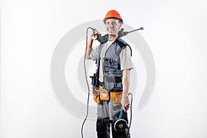 A builder with a hammer drill on his shoulder, and a angle grinder in his other hand, in a helmet, smiles