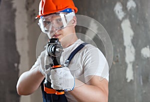 The builder with hammer drill perforator equipment making hole in wall at construction site. Repair work, interior decoration of