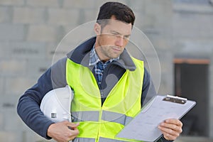Builder in hardhat with clipboard outdoors