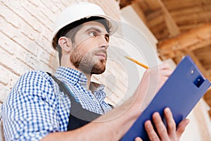 Builder in hardhat with clipboard and pencil indoors