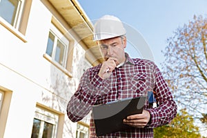 Builder in hardhat with clipboard and pencil outdoors