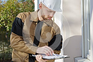 Builder in hardhat with clipboard and pencil outdoors