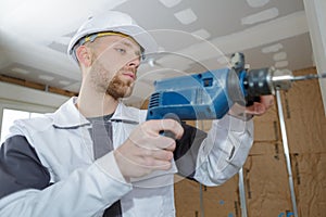 Builder in hardhat perforating wall with drill indoors