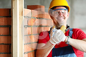 Builder in helmet stands near brickwork and smiles