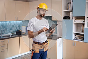 Builder in helmet working with tablet on kitchen background