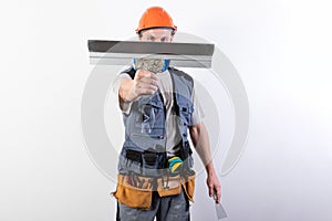 The builder hides his face behind a spatula. In work clothes and hard hat. On a light gray background.