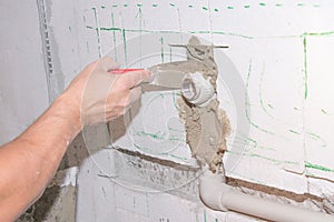 Builder holds a spatula in his hand and covered with cement mortar hole with pipe in the wall