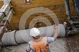 Builder installing big diameter concrete drainage pipe protected by trench support system during deep drainage works