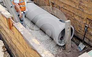 Builder installing big diameter concrete drainage pipe protected by trench support system during deep drainage works