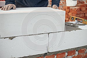 Builder installing masonry white blocks close up. Worker laying autoclaved aerated concrete blocks. Process of house building at