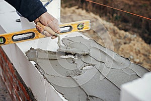 Builder installing masonry white blocks close up. Worker laying autoclaved aerated concrete blocks, working with adhesive and