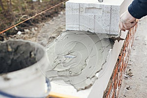 Builder installing masonry white blocks close up. Worker laying autoclaved aerated concrete blocks, working with adhesive and