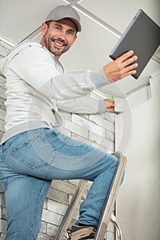 builder on ladder holding tablet