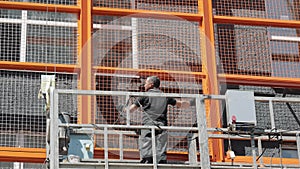 A builder on a lift installs a protective metal mesh on the facade of the house. Decoration of the facade of the house.