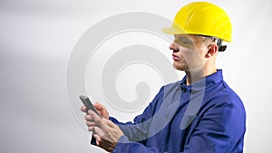 A builder looks at the phone,reads a message,a worker in a yellow helmet on his head,construction worker.On a white background.